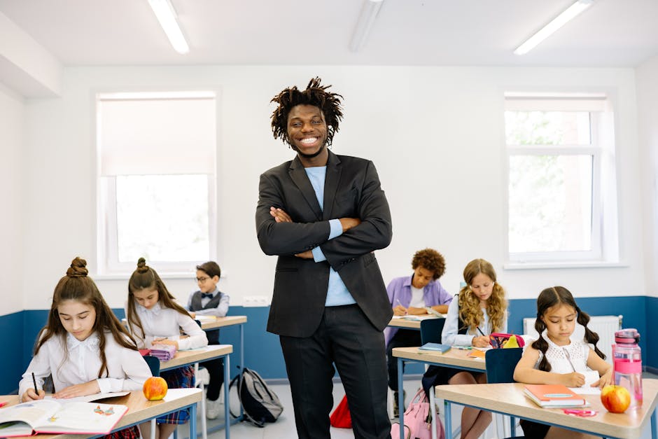 Smiling teacher standing in diverse classroom with students focused on their work.